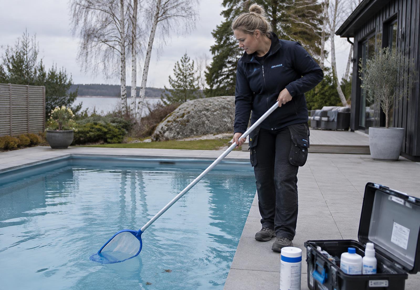 Poolservicetekniker rengör en pool i en nordisk trädgård på våren
